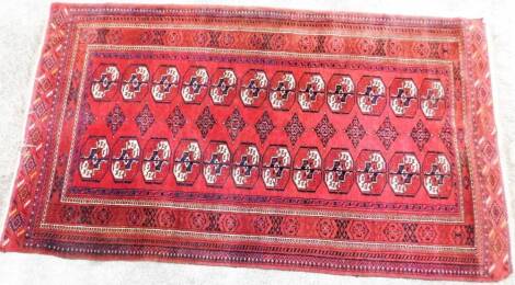 A Persian rug, of rectangular form, in red and blue geometric pattern with floral outline, 226cm x 130cm.