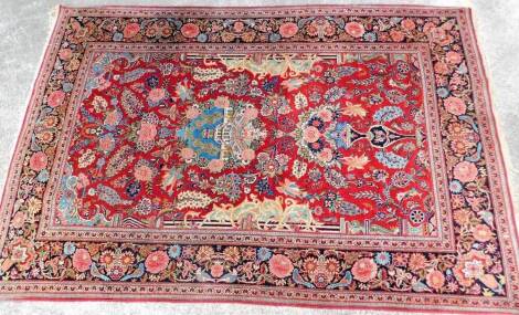 A Persian rug, of rectangular form, decorated with flowers and a geometric pattern, predominately in red, blue and yellow, 210cm x 137cm.