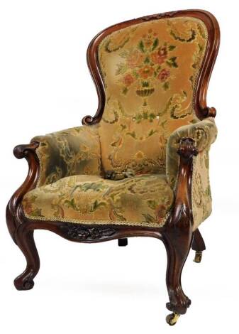 A Victorian mahogany spoon back armchair, with carved floral top, the back arms and serpentine seat upholstered in floral material, on inverted scroll front legs terminating in castors, 112cm H.