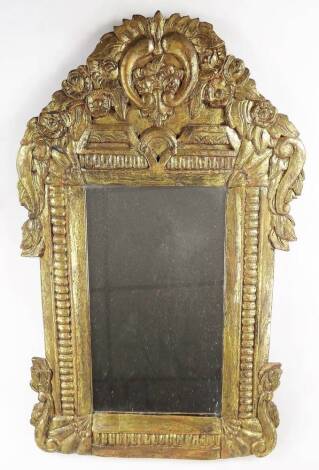 A heavily carved gilt wood mirror, the surround surmounted by scrolls and flowerheads with further scrolls to the sides, with a plain glass and part ring banding broken by floral spandrels, 66cm x 39cm.