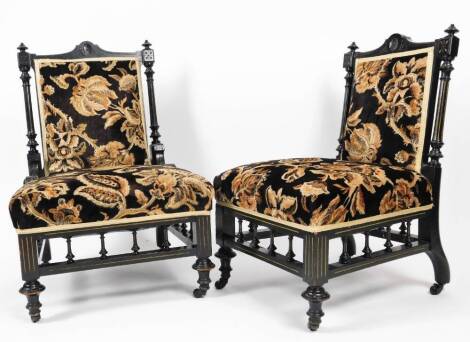 A pair of Victorian ebonised Aesthetic nursing chairs, each with turned backs and overstuffed seats in floral material on turned front legs, terminating in castors,86cm high. (2)