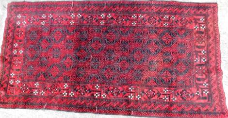 An early 20thC Iranian Blooch Masha hand knotted rug, in red and black geometric pattern, 208cm x107cm.