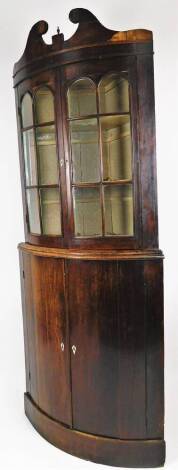 A George III mahogany barrel shaped freestanding corner cupboard, with a broken swan neck pedimented top raised above two arched glazed doors, with double cupboards beneath, on a block base, 211cm H, 80cm W, 53cm D.