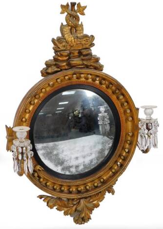 A Regency gilt wood convex mirror, with a circular domed glass, and a heavy bead outline fronted by candle sconces and surmounted by two entwined sea nymphs, on a rock work base, with a carved flowerhead decoration to the under section, 117cm H, 66cm W, 2