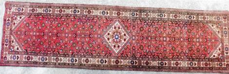 An early 20thC hand knotted runner, probably Middle Eastern, decorated with a geometric floral pattern, predominately in red and blue, 318cm x 88cm.