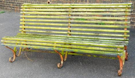 A late 19thC or early 20thC wrought iron and wooden slatted railway style bench, with curved back and seat, on entwined legs, partially painted red, 86cm H, 188cm W, 83cm D.