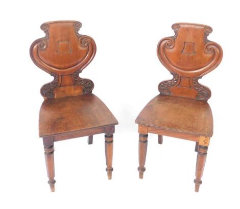 A pair of late Regency mahogany hall chairs, with acanthus leaf carved stylised shield backs, solid seats, raised on turned legs.