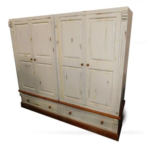 A cream painted pine quadruple wardrobe, with four double panelled doors, opening to reveal two hanging rails, over two long drawers, raised on a plinth base, 194cm H, 221cm W, 57.5cm D.