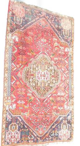 A Qashqai rug, decorated with geometric medallions, birds, and trees, against a red ground, 230cm x 124cm.