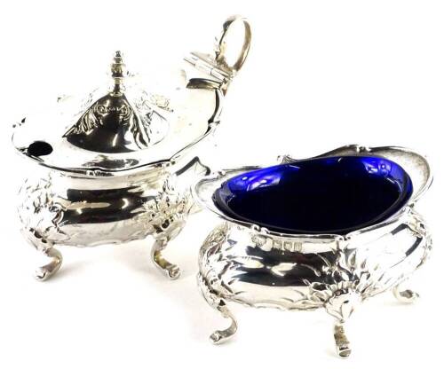 An Edwardian oval silver salt, decorated with shells, scrolls, etc., on four feet, with blue glass liner, and a matching mustard pot, mustard pot lid and one liner (AF), London 1906, 4¼oz.