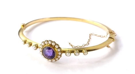 A Victorian amethyst and seed pearl hinged bangle, with circular faceted amethyst stone, surrounded by seed pearls, with three seed pearls to each side, safety chain to clasp, 6.5cm W, 8.1g all in.