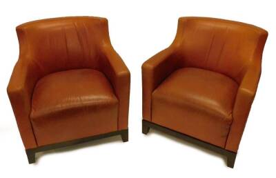 A pair of brown leather armchairs, each on square tapering legs.
