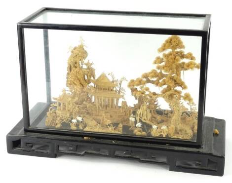 An oriental carved balser and cork display, with trees, storks, buildings, etc., in ebonised case with pierced base, 55cm W.