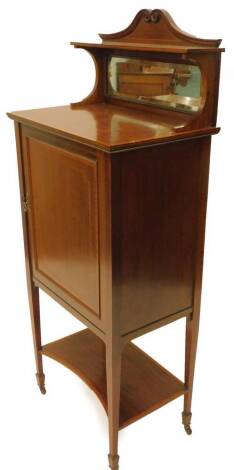 An Edwardian mahogany and satinwood crossbanded music cabinet, the raised back with a shaped crest shelf above a rectangular bevel plate, the base with a single panel door, on square tapering legs with concave under tier, 56cm W.