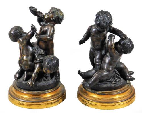 A pair of bronze groups of putti, one featuring a central putto blowing a horn, a second reaching up, a third on all fours beneath, circular base, on a circular brass socle, the other with standing putto holding a leaf, 28cm H.