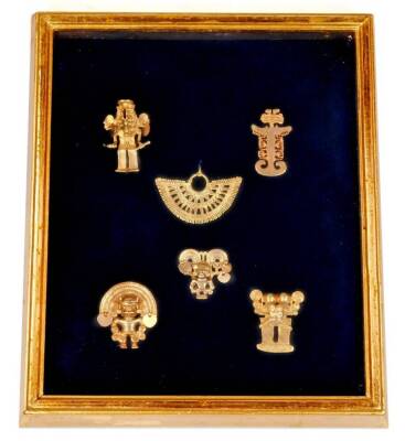 A framed display of six Asian yellow metal trinkets or artifacts.