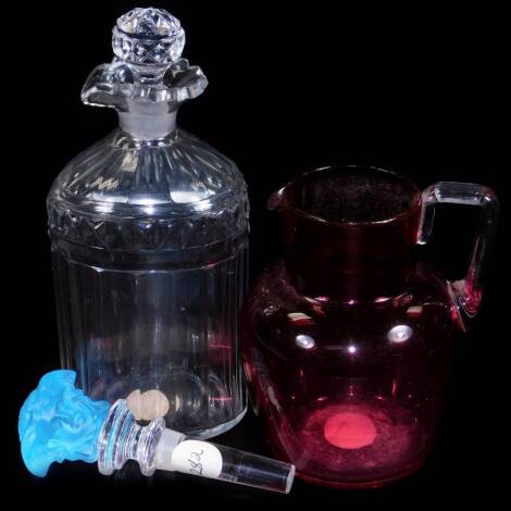 A Rosenthal Versace type clear and frosted glass bottle stopper, with blue glass mask head top,13cm H, a shouldered decanter with stopper, with hobnail cut banding and textured body and a cranberry and clear glass jug with angular handle, unmarked. (3)