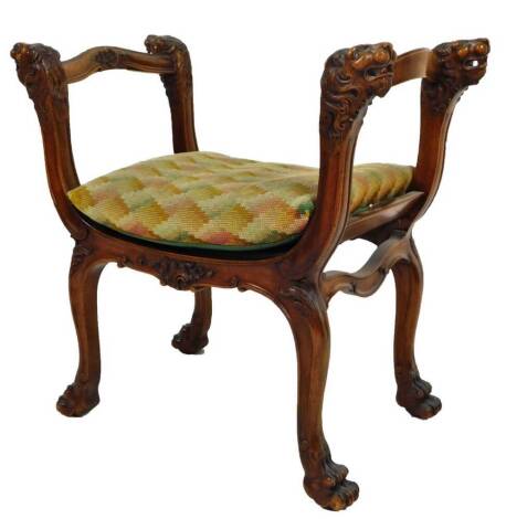 A Regency type mahogany finish stool, with serpentine arm rails, heavily carved lion mask finials, with a carved frieze and hairy paw feet, with material seat and additional cushion, 70cm H, 75cm W, 42cm D.