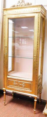 A 20thC French gilt wood display cabinet, surmounted by a ribbon and garland top, with a repeat acanthus leaf banding, the plain glazed door flanked by two glazed panels with faux etching, on turned legs, with a further gilt wood moulding of flowers, scro