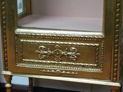 A 20thC French gilt wood display cabinet, surmounted by a ribbon and garland top, with a repeat acanthus leaf banding, the plain glazed door flanked by two glazed panels with faux etching, on turned legs, with a further gilt wood moulding of flowers, scro - 2