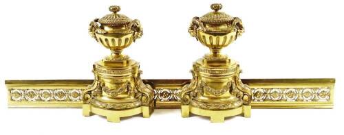 A Regency style metal fire surround, comprising of a pair of andirons surmounted by urns with satyr mask heads, with fixed lids, on acanthus scroll supports and a block base, joined by a rectangular grate front, with a pierced repeat floral pattern, 36cm