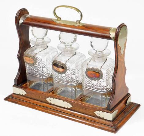 An early 20thC oak tantalus, with three matching bottles, with orb stoppers and silver labels, metal mounts, 37cm H, 37cm W, 16cm D.