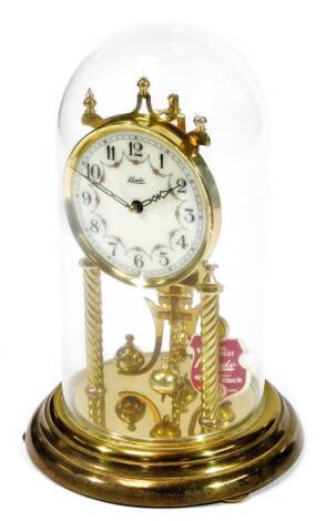 A 20thC Kundo anniversary clock, with triple turned supports, 12cm Dia. Arabic dial decorated with garlands, and visible movement with orb pendulum under a glass dome, 35cm H.