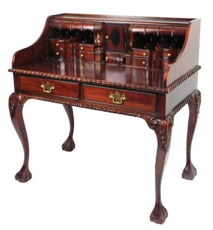 A 20thC mahogany stained writing desk, with a full fitted interior, centred by a cupboard with a shell carving, with a part gadrooned outline, on heavily carved cabriole legs terminating in claw and ball feet, 108cm H, 103cm W, 59cm D.