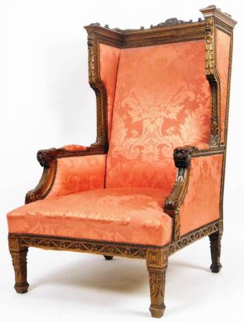 A heavily carved oak wing back throne, with a carved scroll top, overstuffed seat in floral material, heavily carved mask and acanthus leaf arm supports, on square tapering legs, terminating in compressed block feet, 125cm H.