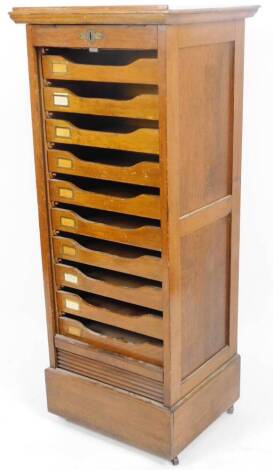 An Edwardian oak filing cabinet, with tambour front revealing an arrangement of ten drawers, with panelled sides, on a block base, 120cm H, 49cm W, 44cm D.