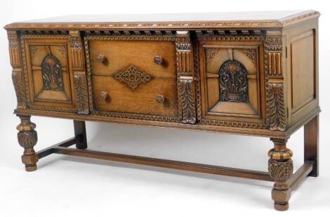 An early 20thC oak sideboard, the heavily carved top raised above two drawers flanked by columns and cupboards on heavy baluster front supports, terminating in block and compressed bun feet, 90cm H, 170cm W, 57cm D.