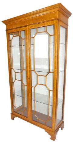 An Edwardian light oak display cabinet, the fixed dentil top raised above an inlaid section and two astragal glazed doors, on ogee bracket feet, with a central three part glazed section, 173cm H, 112cm W, 44cm D.