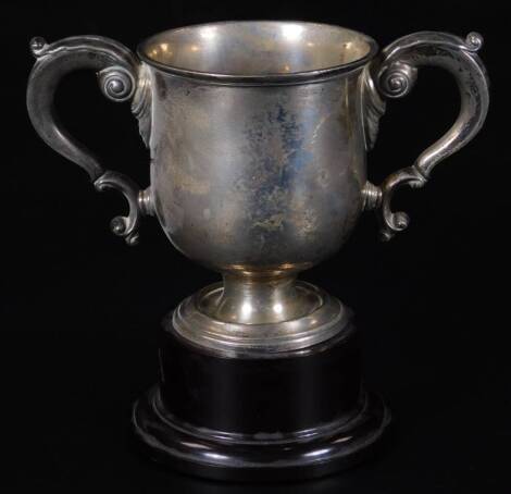 A George V silver trophy, the bell shaped bowl flanked by scroll handles on an ebonised plinth base, Birmingham 1936, 18cm H, 12½oz all in.