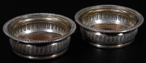 A pair of Elizabeth II silver coasters, each of circular form, with gadrooned outlines, part pierced bodies and wooden bases, with central plain sections, Birmingham 1950, 15cm Dia. (2)