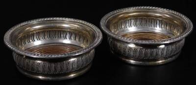 A pair of Elizabeth II silver coasters, each of circular form, with gadrooned outlines, part pierced bodies and wooden bases, with central plain sections, Birmingham 1950, 15cm Dia. (2)