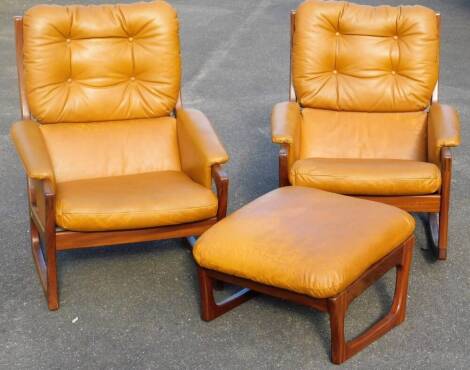 A pair of vintage teak framed armchairs, each with ladder backs and removable button cushions, with overstuffed arms and seat, in brown leather, and a similar footstool, 35cm H, 58cm W, 54cm D. (3)