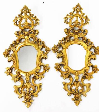 A pair of 20thC gilt wood mirrors, of rococo type, each in heavily carved frames, set with scrolls, flowers, bellflowers, garlands, etc. 93cm H, 43cm W and two gilt wood sconces. (4)