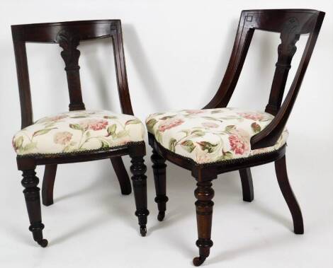 A pair of Edwardian carved dining chairs, each with sloped backs, central carved scroll splats, serpentine seats, turned front legs terminating in castors, overstuffed in floral material, 88cm H.