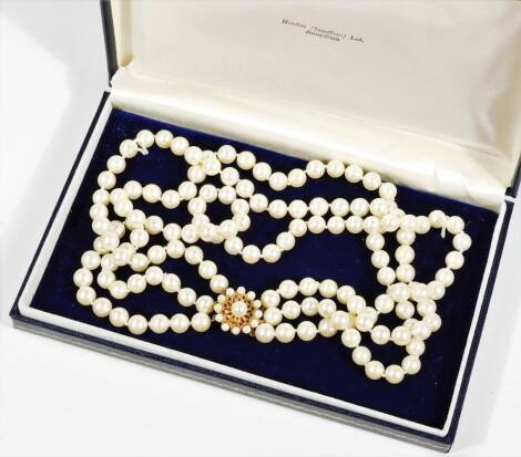 A graduated three row cultured pearl necklace, with 9ct gold clasp set with garnet and cultured pearls in a floral cluster, the clasp 2cm wide, 43cm long overall, 100.5g all in, in Hewitts (Jewellers) Ltd Amersham box.