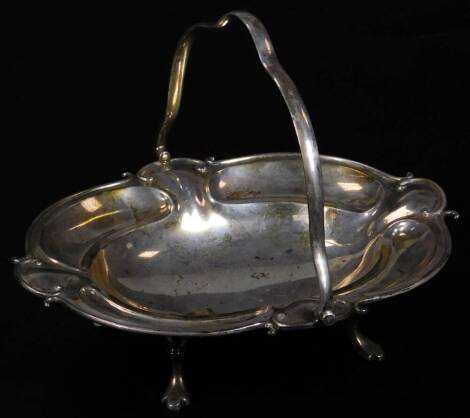 An Edwardian silver cake basket, with shaped swing handle and inverted oval body with a repeat scroll border on quadruple hoof feet, Sheffield, 1910, 26cm W, 20 oz.