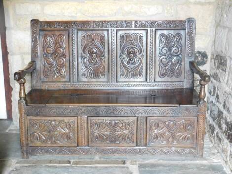 An oak settle, carved 1726 and initialled MB, the four panelled back heavily carved with scrolls and flowers, above a log box seat and three panelled front, with shaped arms on turned baluster supports, 113cm H, 147cm W, 59cm D.