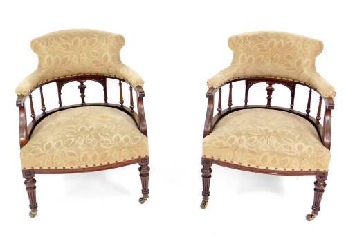 A pair of late Victorian walnut tub chairs, with spindle and scratch carved gallery backs, over stuffed seats, and fluted legs with castors.