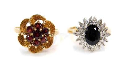 A 9ct gold sapphire and diamond flower head ring, together with a 9ct gold and garnet flower head ring in a textured repeating curl mount, sizes N 1/2 and R 1/2 respectively, 7.4g all in.