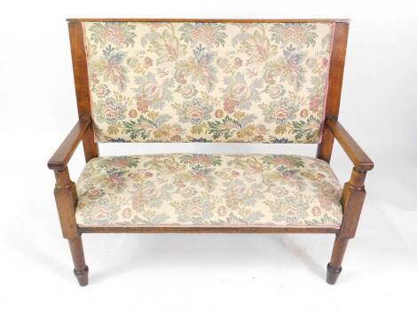An oak two seater settle, with over stuffed upholstered seat and back, decorated in floral upholstery, raised on turned legs, 112cm W.