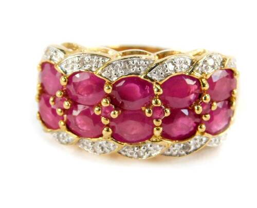 A 9ct gold ruby and diamond ring, set with ten rubies in two rows, flanked by diamond set curls in a four row pleated design, size P 1/2, 4.4g. (boxed)