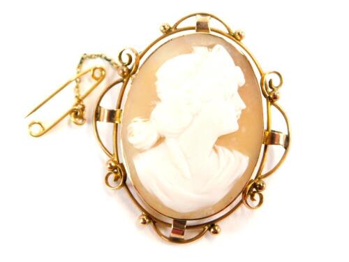 An early 20thC shell cameo brooch, the shell cameo depicting a maiden looking right in a gold scroll work frame, stamped 9c, with safety chain, 4cm x 5cm, 9.5g all in.