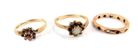 Three 9ct gold dress rings, comprising two floral clusters, one set purely with garnets, the other set with garnets and imitation opal, and an eternity ring set with CZ stones (AF), 5.4g.
