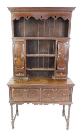 An early 20thC cottage style oak dresser, the outswept pediment over a backed three shelf plate rack, flanked by cupboards and two small drawers, over two deep drawers, raised on turned legs united by stretchers, 201cm H, 105cm W, 45cm D.