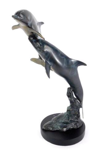 A patinated bronze sculpture modelled as dolphins, swimming from a rocky base, on a circular stand, 45cm H.