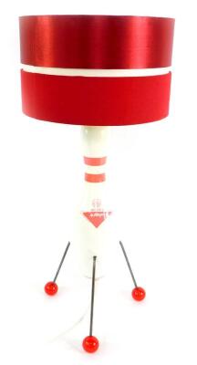 An Atomic style table lamp, the body formed as a ten pin bowl Amflite II, raised on three metal rod legs, with ball feet, and red banded cylindrical shade, 69cm H.